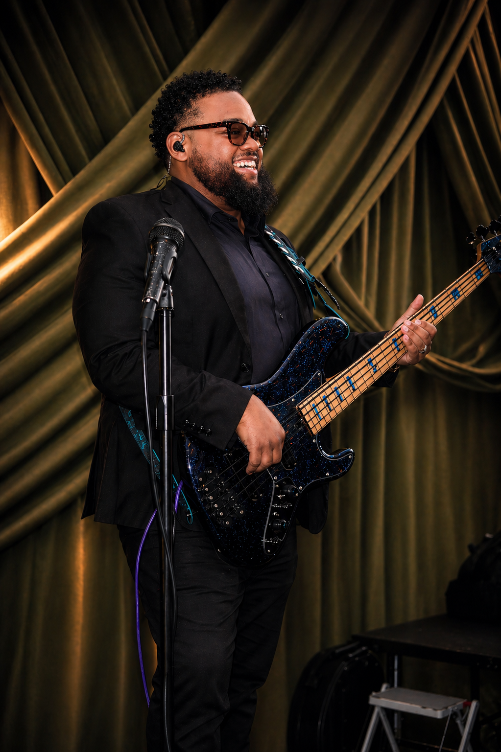 Benjamin Parker performing on stage with bass guitar in front of gold curtains